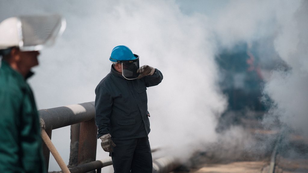 Operarios con protección respiratoria trabajando entre humos en una instalación industrial